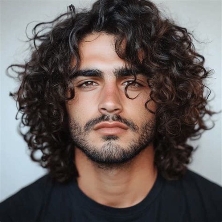 a man with curly hair wearing a black tank top and looking at the