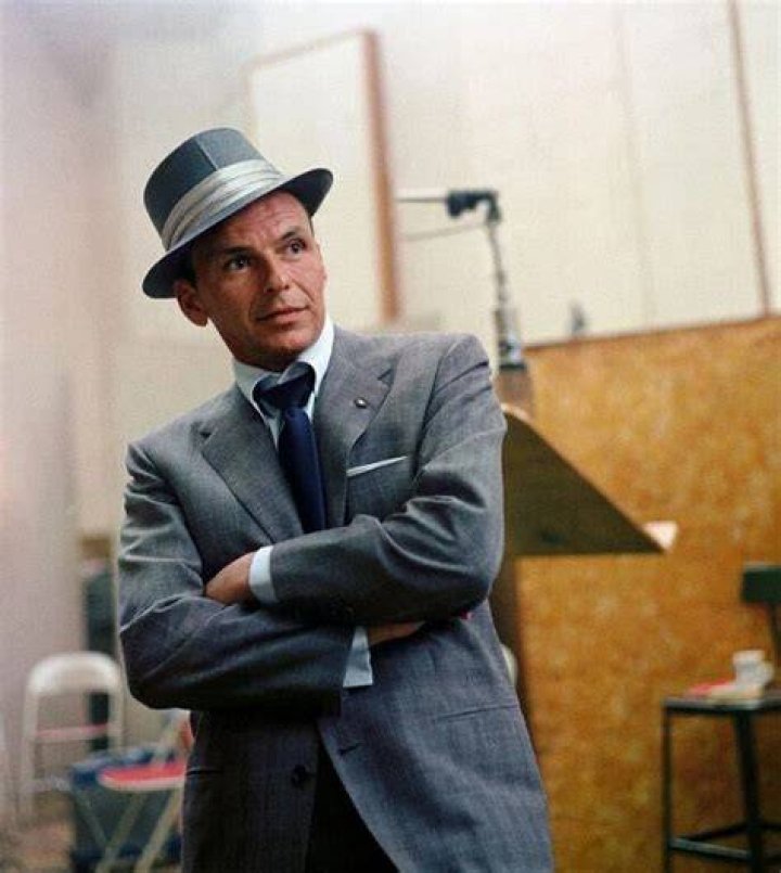 Frank Sinatra wears a suit and sits in front of a red background.
