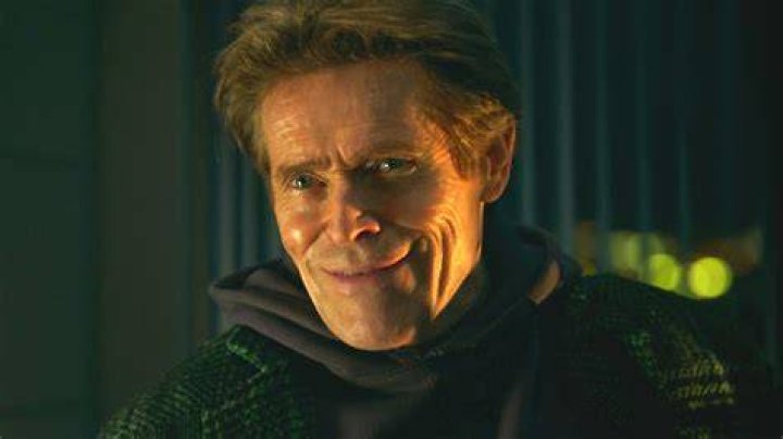 Green Goblin actor Willem Dafoe at the premiere of 'Spider-Man: No Way Home.' He's wearing a black suit and smiling.