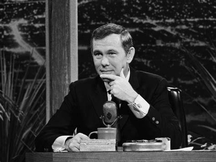 Johnny Carson in black, seated next to second wife, Joanne Carson, who is laughing