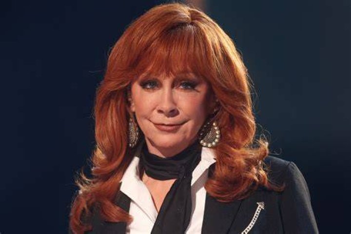 Reba McEntire in a dark blue dress holding a microphone