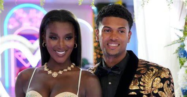Zeta Morrison and Timmy Pandolfi, who will appear at the 'Love Island USA' Season 4 reunion, embrace one another. Zeta wears a white dress. Timmy wears a black and gold patterned suit.