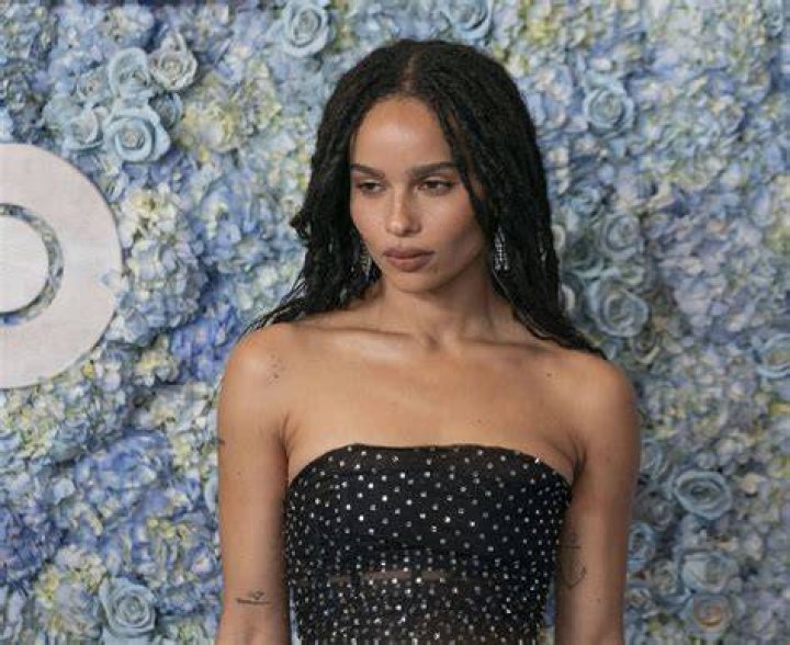 Zoe Kravitz poses in front of a large red sign that says "The Batman."